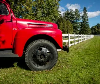Red utility truck parked on grass in front of a white fence enveloping trees