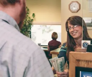 Smiling female Union Bank teller with glasses hands a bearded male customer cash