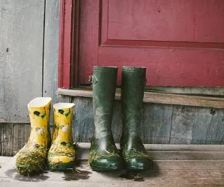 Two pairs of dirty work boots sitting in front of a red door