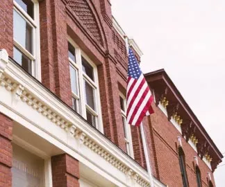 American flag raised over the facade of a historic red brick building